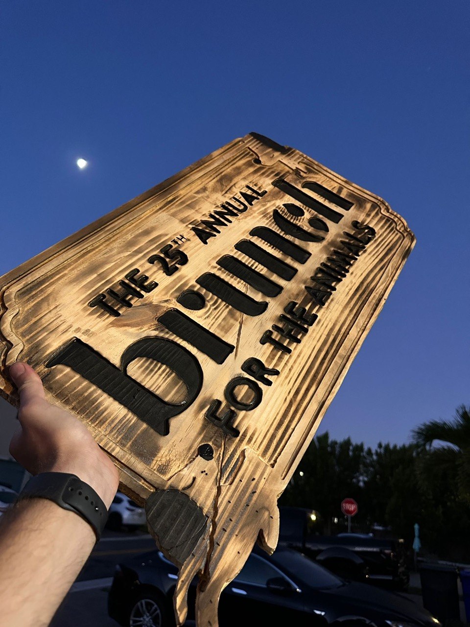 CNC routed burnt wood event sign photographed at dusk