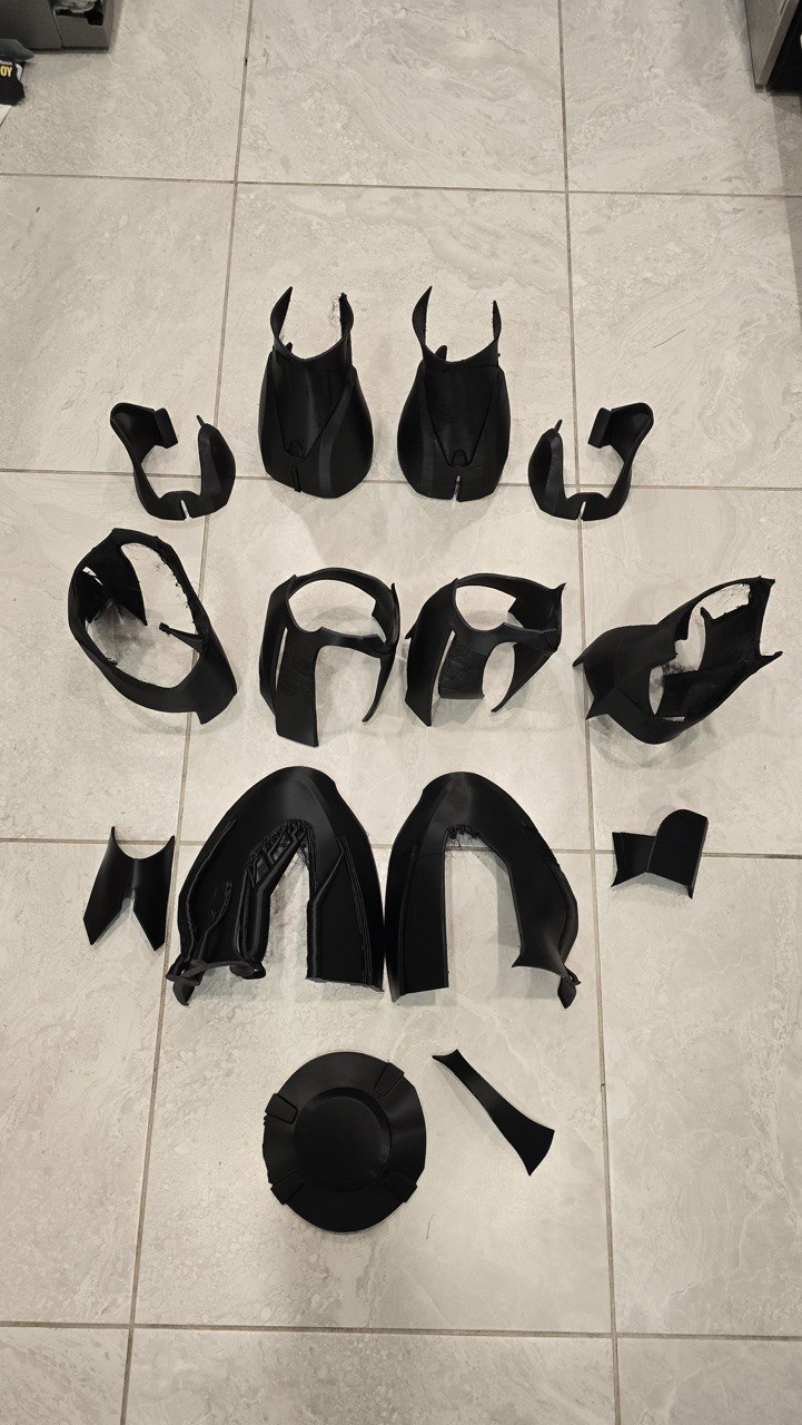 Sixteen black 3D printed cosplay armor shell pieces laid out