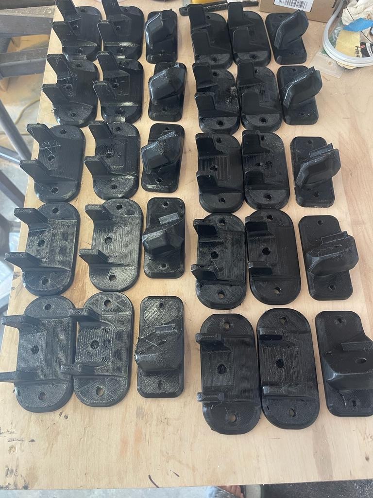 Batch of thirty black 3D printed mounting brackets on a workbench
