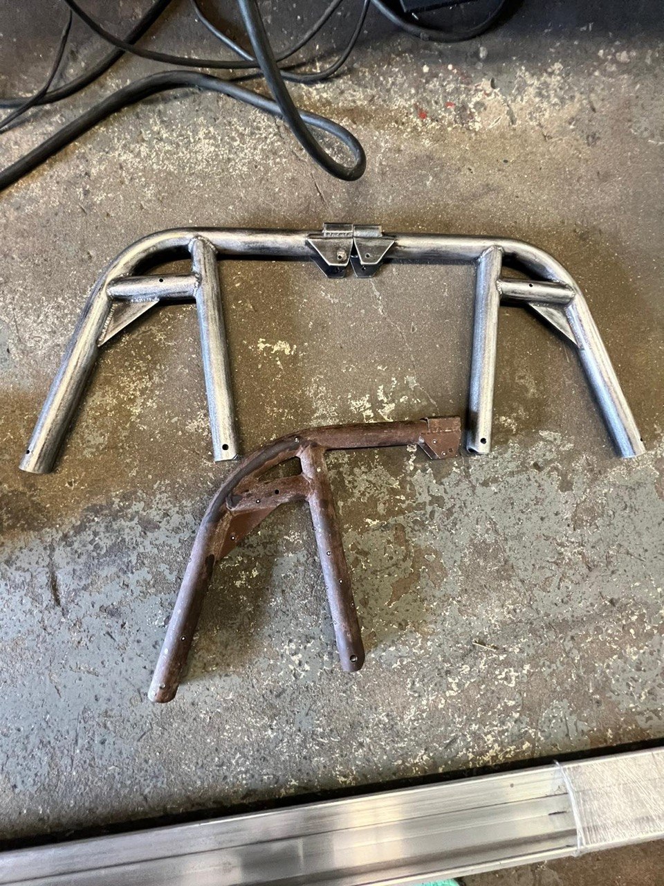 Rusted original roll bar beside a newly fabricated polished replacement